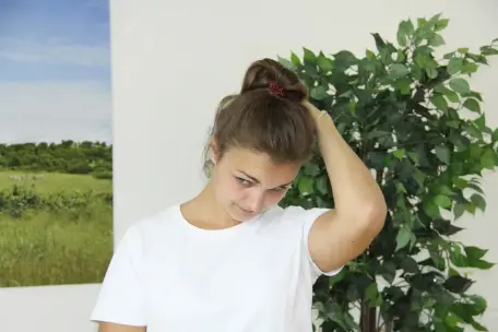 Žena provádí úklon hlavy s rukou přes temeno při protažení svalů kolem páteře.