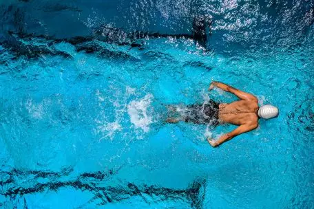 Plavec s bílou čepicí plave kraul v bazénu při sportovním tréninku.