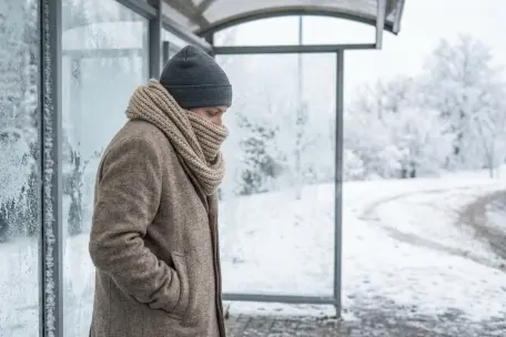 Muž čekající v zimně na autobus, schoulené držení těla.