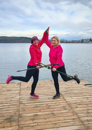 Dvě instruktorky Nordic Walkingu v růžovém s holemi si na dřevěném molu u jezera dávají pětku